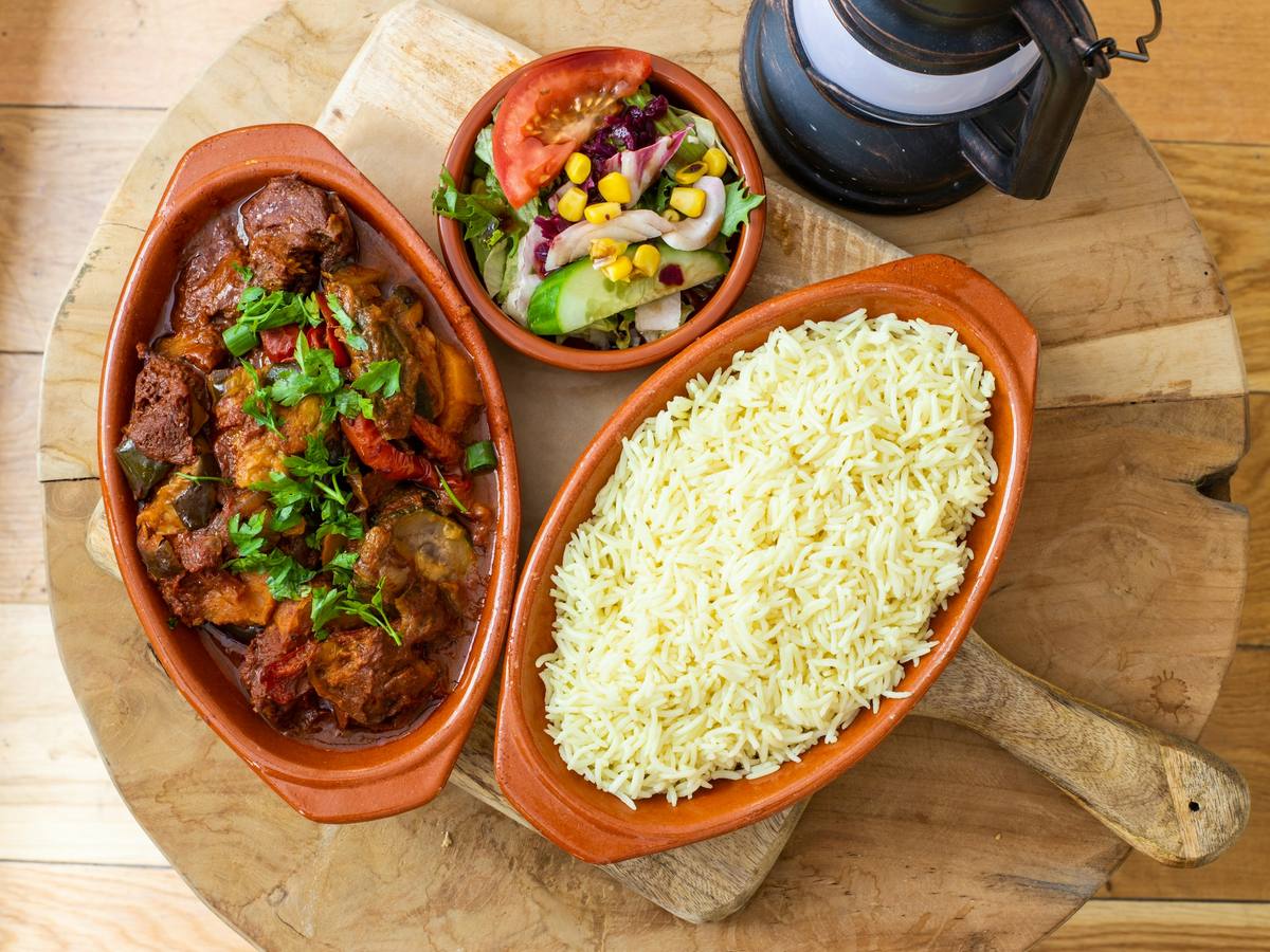 Ensopado de carne com legumes e arroz branco em travessas de barro sobre tábua de madeira, com salada ao lado