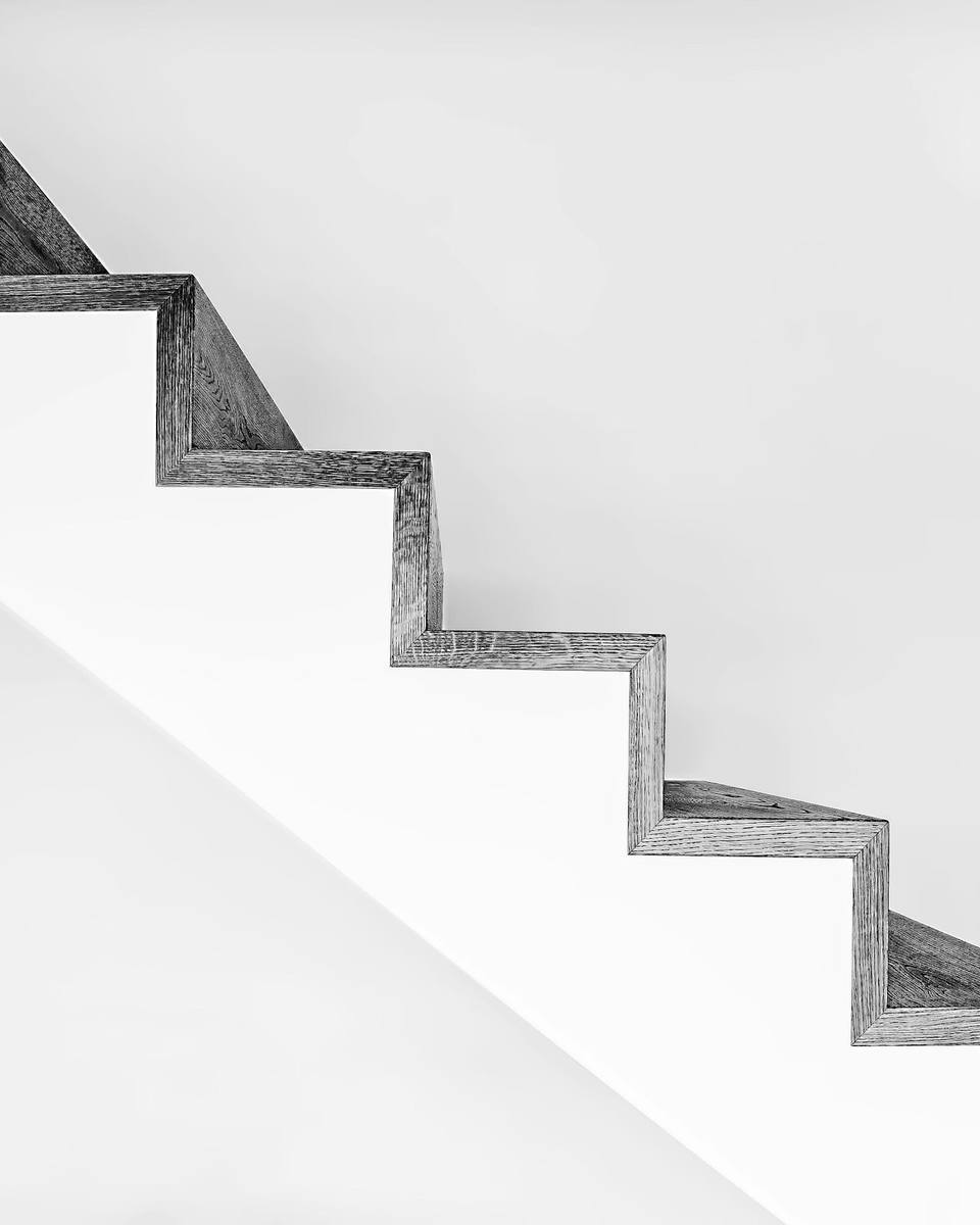 Escada de degraus brancos com perfil escuro, vista de lado contra parede branca